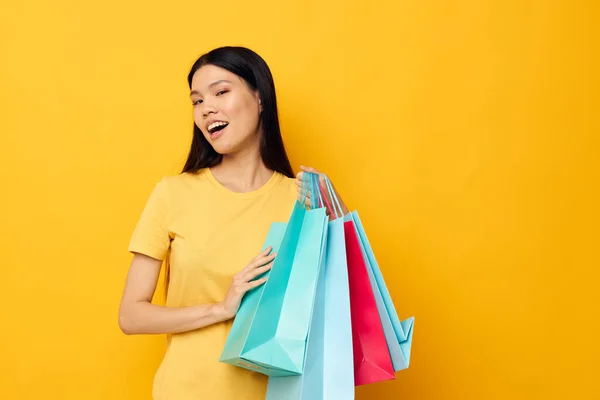 Charmante jonge Aziatische vrouw in een geel T-shirt met veelkleurige boodschappentassen studio model ongewijzigd — Stockfoto