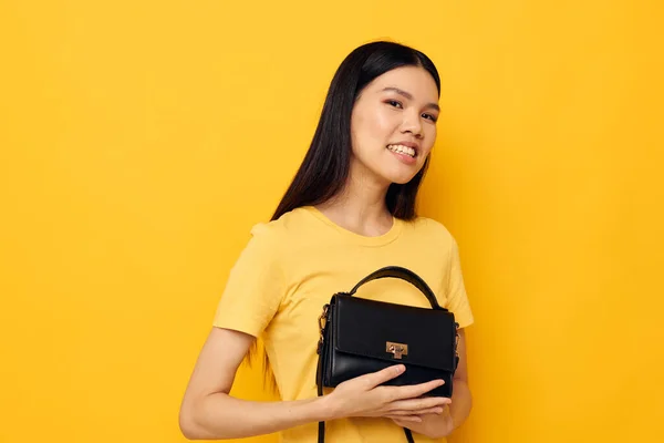 Cheerful woman in a yellow t-shirt black womens bag — Stockfoto
