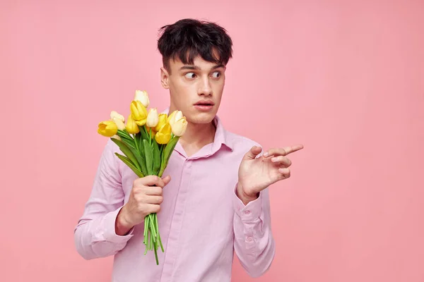 Hombre bonito en una camisa rosa con un ramo de flores haciendo gestos con sus manos fondo rosa inalterado — Foto de Stock