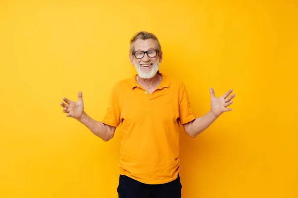 Portrait elderly man posing yellow tshirt glasses yellow background — ストック写真