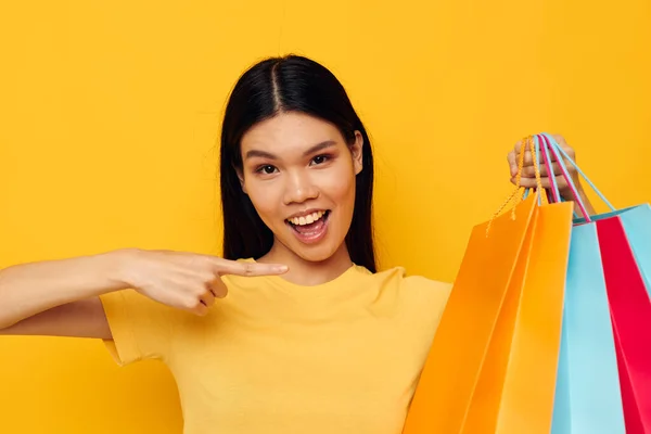Pretty brunette in a yellow T-shirt with multicolored shopping bags yellow background unaltered — Stockfoto