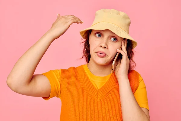 Смешная девушка в оранжевом свитере в желтой шляпе разговаривает по телефону розовый фон без изменений — стоковое фото