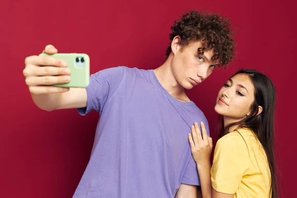 빨간 핸드폰 배경의 다채 로운 티셔츠를 입은 젊은 남성 과 소녀 — 스톡 사진