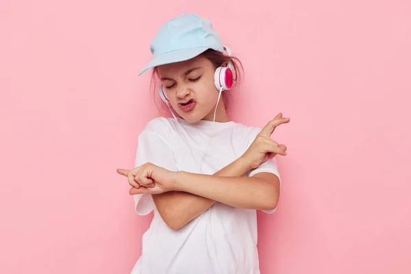 Portrait of happy smiling child girl headphones in a white t-shirt and a cap pink background — Stockfoto