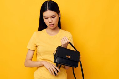 Elinde siyah kadın çantası olan yakışıklı Asyalı genç bir kadın. Sarı arka planı değişmemiş.