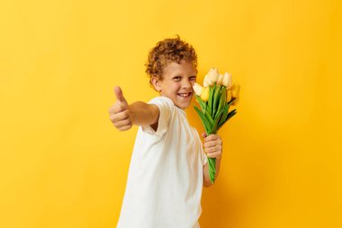 Çiçek buketi olan beyaz tişörtlü küçük bir çocuk. Stüdyonun izole edilmiş bir arka planı var.