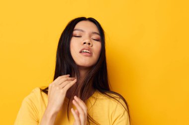 Sarı tişörtlü çekici genç Asyalı kadın. Kafasını tutuyor. Sarı arka planı değişmemiş.