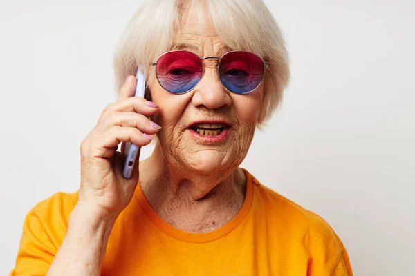 Sıradan tişörtlü, güneş gözlüklü, telefon ışığı arka planında konuşan yaşlı bir kadının portresi. — Stok fotoğraf