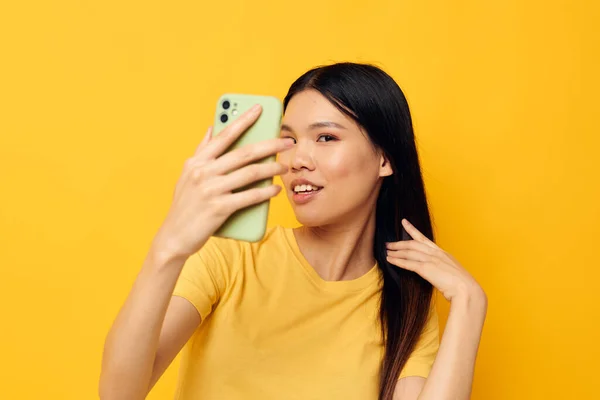 Pretty brunette with a phone in her hands makes a selfie yellow background unaltered — Foto Stock