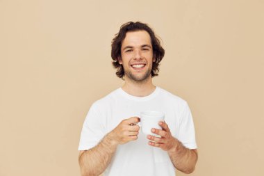 Elinde beyaz bir kupayla çekici bir adam. Duyguları bej arka planda.
