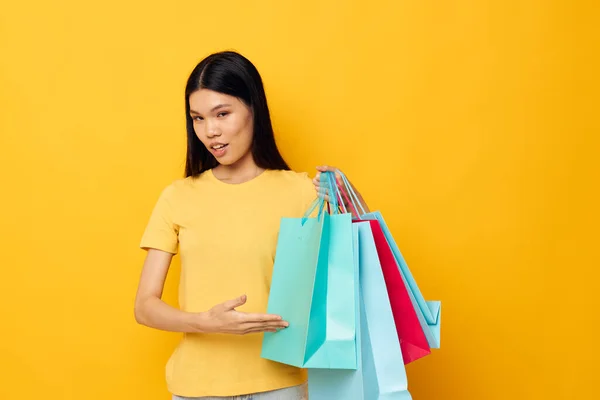 Vrouw met aziatische uitstraling in een geel T-shirt met veelkleurige boodschappentassen studio model ongewijzigd — Stockfoto