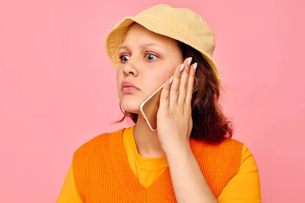 Drôle fille dans un pull orange en chapeau jaune parler sur le téléphone fond rose inchangé — Photo