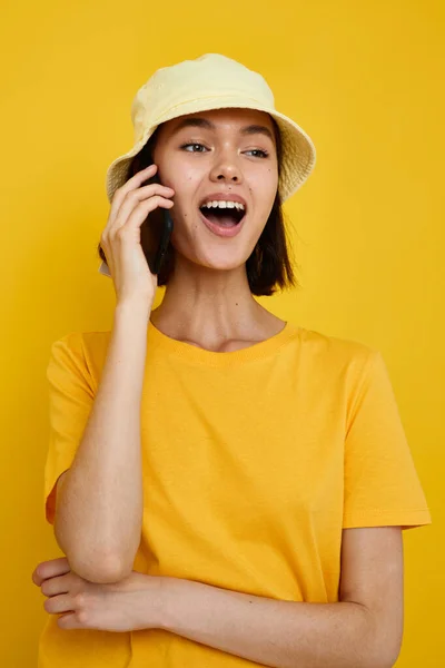 Νεαρή γυναίκα κίτρινο t-shirt και καπέλο καλοκαιρινό στυλ με τηλέφωνο κίτρινο φόντο — Φωτογραφία Αρχείου