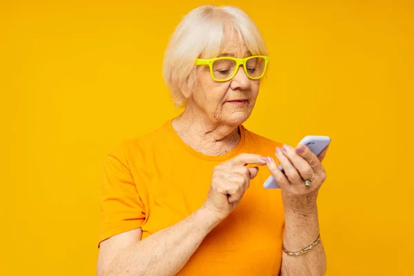Sonriente anciana feliz estilo de vida en camisetas amarillas con el teléfono de fondo amarillo — Foto de Stock