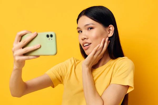 Γοητευτική νεαρή Ασιάτισσα με ένα κίτρινο μπλουζάκι κοιτάζοντας το τηλέφωνο παριστάνοντας τον τρόπο ζωής αναλλοίωτο. — Φωτογραφία Αρχείου