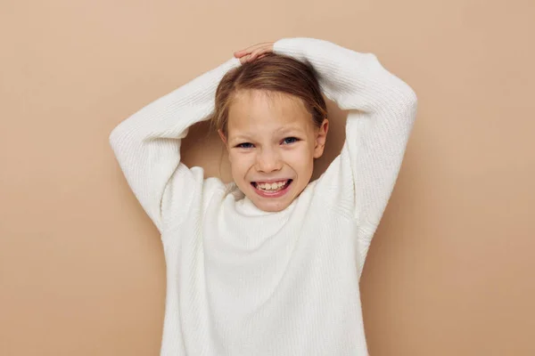 Portrét šťastné usměvavé dítě dívka v bílém svetru pózuje rukou gesta béžové pozadí — Stock fotografie