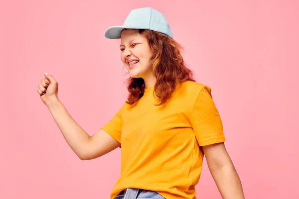 Beautiful woman in a yellow t-shirt and blue cap posing emotions pink background unaltered — Stockfoto