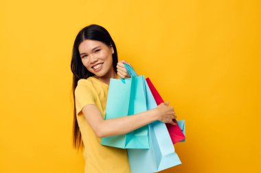 Sarı tişörtlü, çok renkli alışveriş çantalı yakışıklı genç Asyalı kadın. Stüdyo modeli değiştirilmemiş.