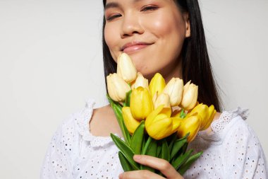 Beyaz gömlekli, çekici bir Asyalı kadın. Çiçekler bahar. Stüdyo modeli gibi poz veriyor.