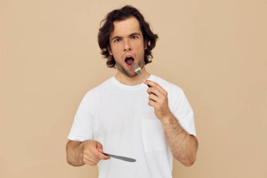 Çatal bej arka planı olan beyaz tişörtlü yakışıklı bir adam.