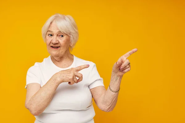 Photo of retired old lady in casual t-shirt gestures with his hands yellow background — Stock Photo, Image