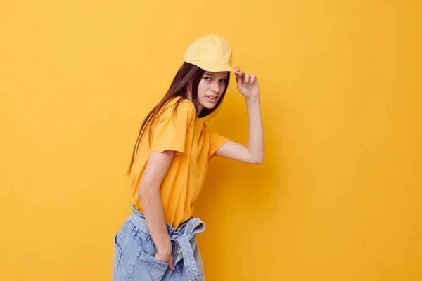 Ung vacker kvinna poserar i en gul T-shirt och mössa gul bakgrund — Stockfoto