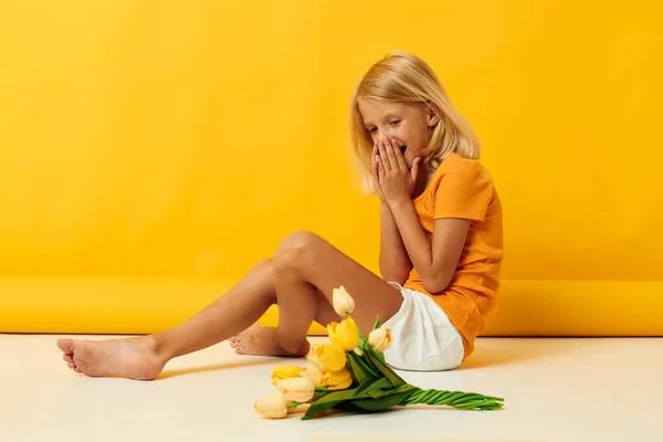 Niña sentada en el suelo con un ramo de flores de fondo amarillo — Foto de Stock