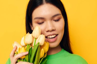 Asyalı görünümlü yeşil tişörtlü bir buket sarı çiçekli arka planda değişmemiş bir kadın.