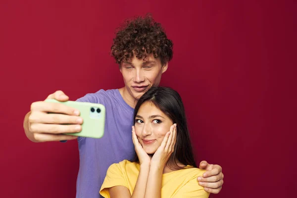 Bel ragazzo e ragazza in t-shirt colorate con uno sfondo isolato telefono — Foto Stock