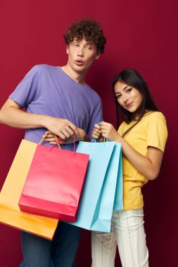 Renkli tişörtler içinde sevimli genç bir çift çantalarla izole edilmiş arka plan alışverişi yapıyorlar.