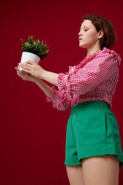 Ayakta duran ve elinde çiçekle kırmızı arka planda genç bir kadın.