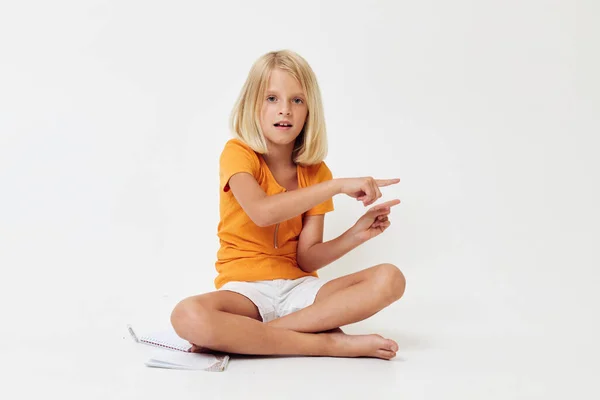 Mała dziewczynka z blond włosami gestykulująca rękami siedząc na podłodze — Zdjęcie stockowe