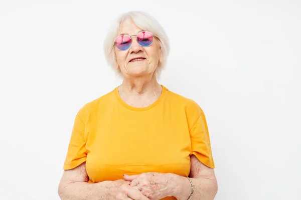 Smiling elderly woman in a yellow t-shirt posing light background — Zdjęcie stockowe