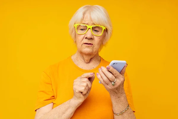 Anciana feliz estilo de vida en camisetas amarillas con el teléfono de fondo amarillo — Foto de Stock