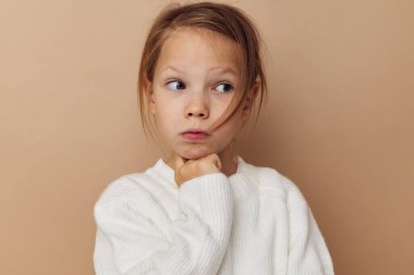 Beyaz kazaklı güzel bir genç kız. El hareketleriyle bej arka planda.