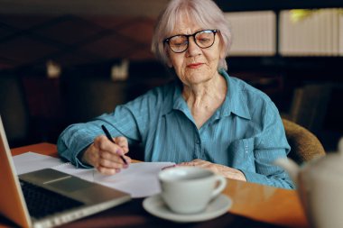Gözlüklü yaşlı bir kadın dizüstü bilgisayarın önünde oturuyor. Sosyal ağlar değiştirilmemiş.