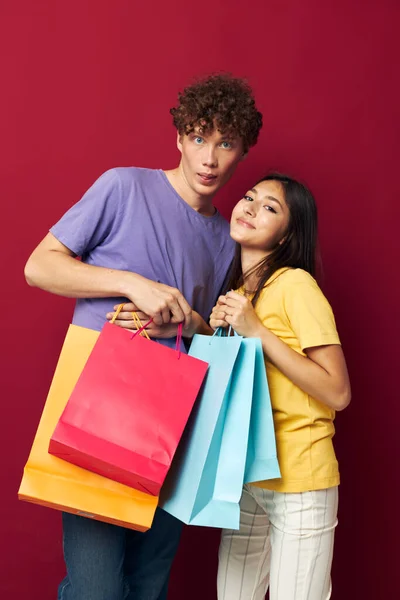 Cute young couple in colorful T-shirts with bags Shopping isolated background unaltered — Stockfoto