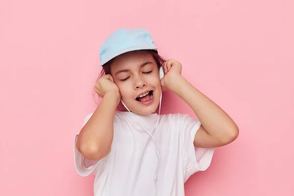 Niedliche Mädchen Kopfhörer in einem weißen T-Shirt und einer Mütze rosa Hintergrund — Stockfoto