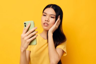 Sarı tişörtlü güzel esmer. Telefona bakıyor. Arka planda bir değişiklik yok.