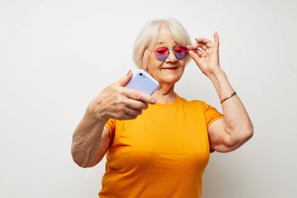 Πορτρέτο μιας ηλικιωμένης φιλικής γυναίκας σε ένα κίτρινο t-shirt που θέτουν την επικοινωνία από το τηλέφωνο περικοπεί άποψη — Φωτογραφία Αρχείου
