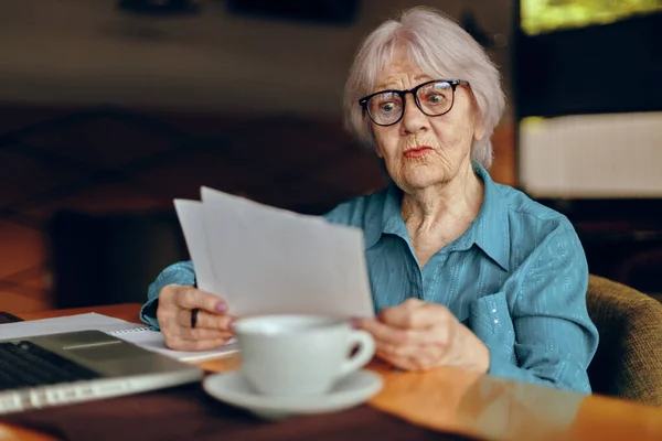 Retrato de una anciana sentada en un café con una taza de café y un portátil Freelancer funciona sin alteraciones — Foto de Stock