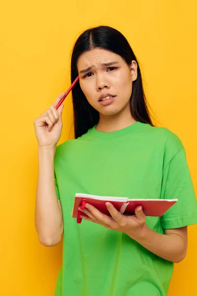 Femme avec apparence asiatique T-shirts verts avec carnet rouge et stylo fond jaune inchangé — Photo