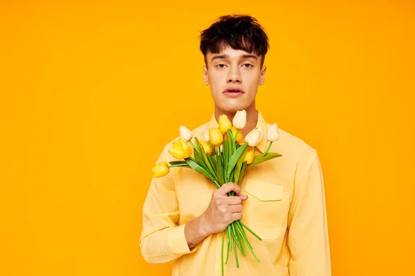 Chico guapo en gafas amarillas con un ramo de flores fondo amarillo inalterado — Foto de Stock