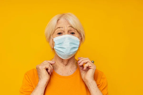 Tıbbi maskeli, sarı tişörtlü yaşlı bir kadın duygularını kapatıyor. — Stok fotoğraf