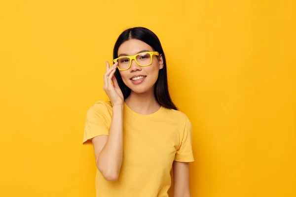 Woman with Asian appearance in yellow t-shirts with glasses posing fashion yellow background unaltered — Fotografia de Stock