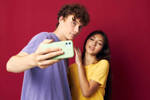 Bel ragazzo e ragazza in t-shirt colorate con uno sfondo rosso telefono — Foto Stock