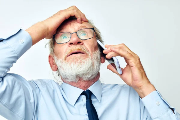 Starý muž s telefonem šokován ve studiu na bílém pozadí — Stock fotografie