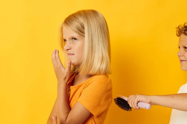 A boy with a comb combing a girls hair yellow background — Stock Photo, Image