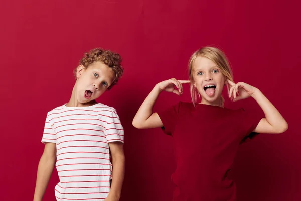 Милые дошкольники улыбаются и позируют в повседневной одежде на красном фоне — стоковое фото