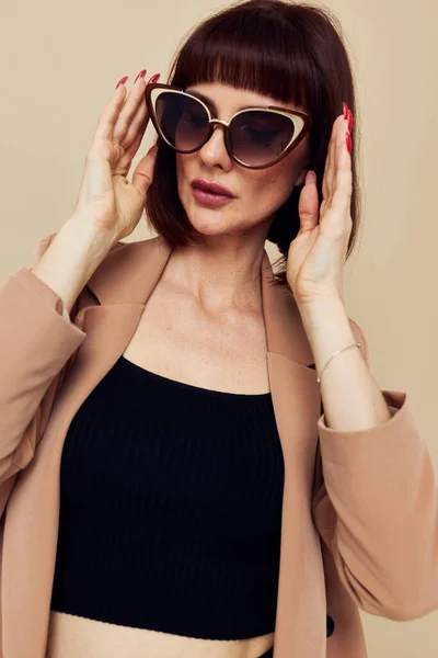 Foto mulher bonita em óculos de sol terno de cabelos curtos gestos com as mãos luz de fundo — Fotografia de Stock